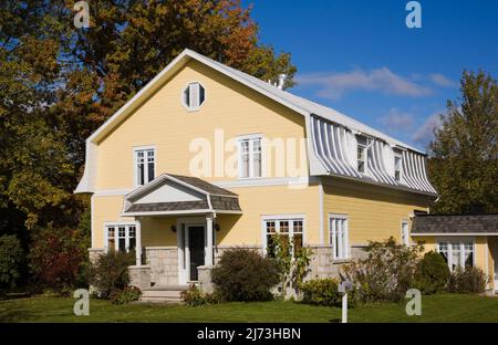 Gelbes zweistöckiges Haus mit Stein- und Holzplanken im Scheunenstil mit landschaftlich gestaltetem Vorgarten im Herbst. Stockfoto