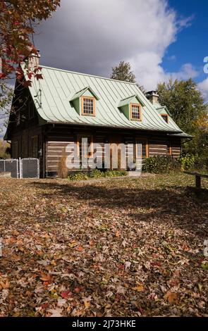 Altes Blockhaus im kanadischen Stil aus dem Jahr 1800s mit landschaftlich gestaltetem Vorgarten im Herbst. Stockfoto