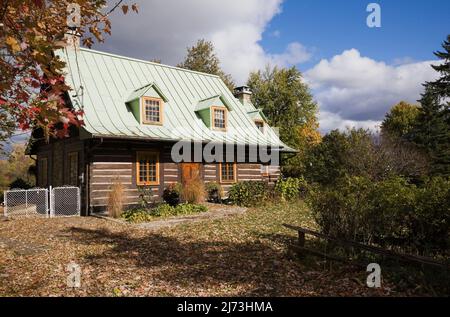 Altes Blockhaus im kanadischen Stil aus dem Jahr 1800s mit landschaftlich gestaltetem Vorgarten im Herbst. Stockfoto