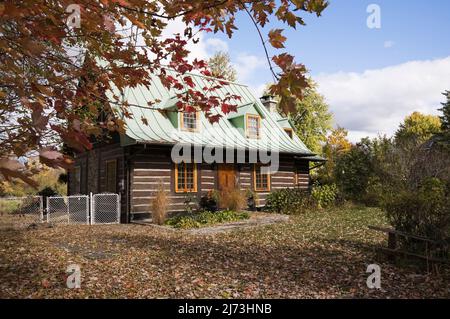 Altes Blockhaus im kanadischen Stil aus dem Jahr 1800s mit landschaftlich gestaltetem Vorgarten im Herbst. Stockfoto