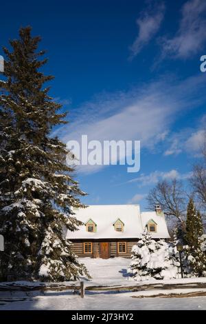 Altes Blockhaus im kanadischen Stil aus dem Jahr 1800s, das im Winter durch einen rustikalen Holzzaun geschützt ist. Stockfoto