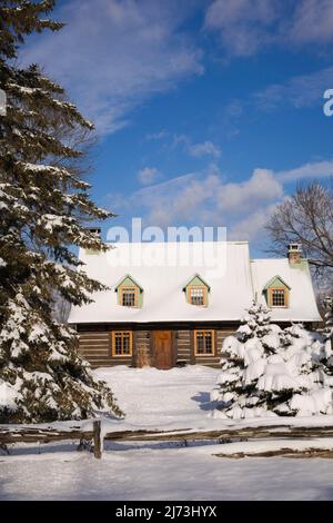 Altes Blockhaus im kanadischen Stil aus dem Jahr 1800s, das im Winter durch einen rustikalen Holzzaun geschützt ist. Stockfoto