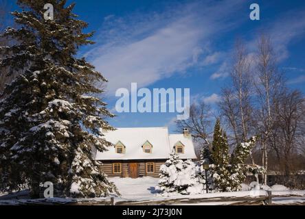 Altes Blockhaus im kanadischen Stil aus dem Jahr 1800s, das im Winter durch einen rustikalen Holzzaun geschützt ist. Stockfoto