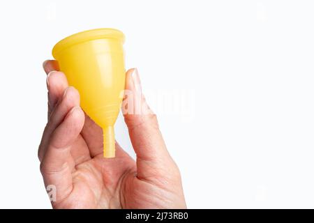 Hand mit einer gelben Menstruationsschale auf weißem Hintergrund. Frauengesundheitskonzept. Umweltfreundliches Konzept. Zero Waste Konzept. Stockfoto