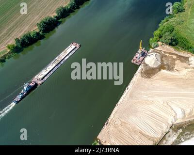 Kleines Schleppboot schiebt Barge entlang ruhigem Wasser vorbei an Feldern Stockfoto