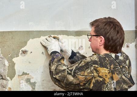 Entfernen von Farbe von der Wand mit einem Schaber, Reparatur des Raumes Stockfoto