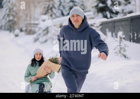 Lächelnder Mann, der der Frau eine Schlittenfahrt gibt. Liebe und Freizeit Konzept. Hochwertige Fotos Stockfoto