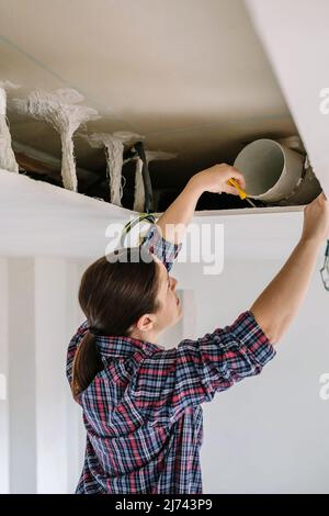 Frau, die Rohr für die Installation der Küchenhaube platziert Stockfoto