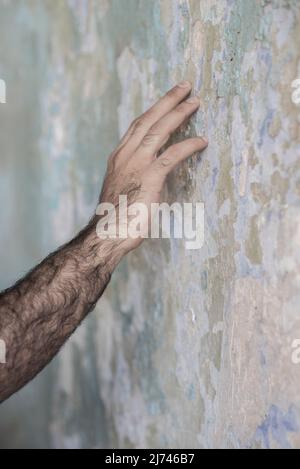 Nahaufnahme der Hand eines Mannes, der die geschälte Wandfarbe berührt Stockfoto