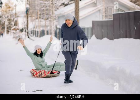 Lächelnder Mann, der der Frau eine Schlittenfahrt gibt. Liebe und Freizeit Konzept. Hochwertige Fotos Stockfoto