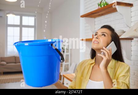 Frau mit beschädigtem Dach und undichter Decke in ihrem Haus ruft den Reparaturservice an Stockfoto