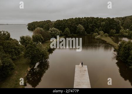 Europäischer kaukasischer Bräutigam im Anzug und schwarzhaarige Braut im weißen Hochzeitskleid mit langem Schleier und Tiara auf dem Kopf. Brautpaar küsst sich umarmt Stockfoto