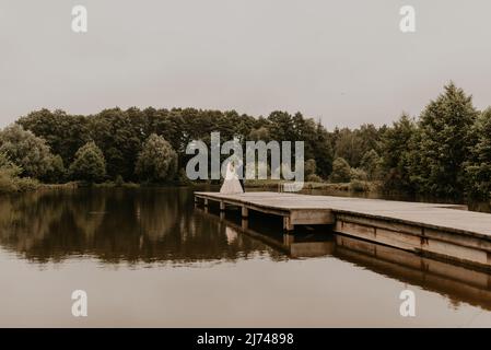 Blonde europäische kaukasische junge Mann Bräutigam in blauem Anzug und schwarzhaarige Frau Braut in weißem Hochzeitskleid mit langem Schleier und Tiara auf dem Kopf. Frisch Vermählt Stockfoto