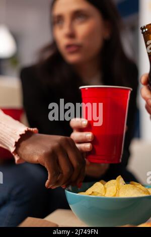 Büroangestellte haben Spaß mit alkoholischen Getränken und Chips bei der Feierlichkeit nach der Arbeit. Kollegen genießen Bier in Flaschen und Gläsern, essen Snacks und lachen nach Stunden zusammen. Nahaufnahme. Stockfoto