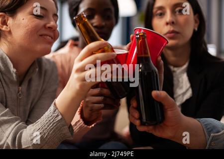 Geschäftsleute klirren nach der Arbeit auf einer Party im Büro auf Gläser und Bierflaschen. Freunde treffen sich, um nach der Arbeit einen Drink zu genießen und feiern mit Jubel. Nahaufnahme. Stockfoto