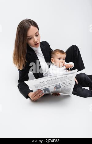 Junge Geschäftsfrau liest Zeitung in der Nähe von kleinen Sohn auf weiß Stockfoto