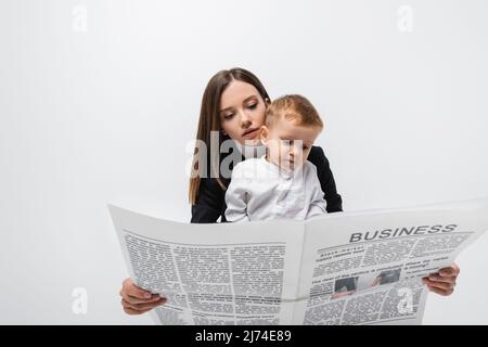 Junge Geschäftsfrau liest Zeitung in der Nähe Kleinkind Kind auf grau isoliert Stockfoto