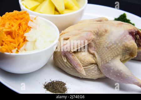 Frisches rohes Bio-Wachtelfleisch mit Zutaten zum Kochen gesunder Suppe. Roher Wachtelvögel, frisch geschnittene Kartoffeln, Karotten, Zwiebeln, gefrorene Petersilie und Gewürzen auf t Stockfoto