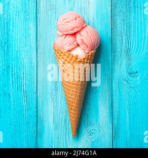 Erdbeereis in einem Waffelkegel auf blauem Hintergrund. Stockfoto