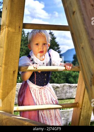 Mädchen in traditioneller bayerischer/österreichischer Kleidung klettert auf einer Rutsche Stockfoto