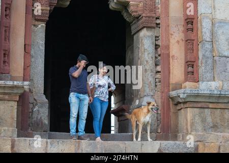 Junges Paar geht steinerne Treppen hinunter mit einem streunenden Hund durch einen verzierten bogigen Eingang an einem historischen Denkmal in Indien Stockfoto