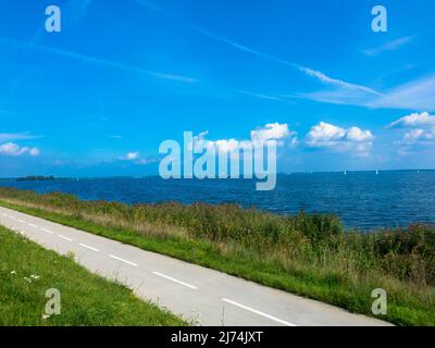 Radweg oder Wanderweg mit grünem Gras auf dem Deich mit blauem Himmel. Mitten in der Natur. Ijsselmeer, Niederlande Stockfoto