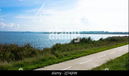 Radweg oder Wanderweg mit grünem Gras auf dem Deich mit blauem Himmel. Mitten in der Natur. Ijsselmeer, Niederlande Stockfoto