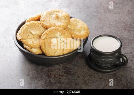 Weiße Schokolade Karamell weich und Macadamianüsse gebackene Kekse mit einer Tasse Milch auf dem Tisch close-up serviert. Horizontal Stockfoto