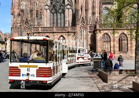 Straßburg, Frankreich - April 2022: Menschen an Bord eines touristischen Landzuges im Stadtzentrum. Im Hintergrund befindet sich die Kathedrale Notre-Dame de Strasbourg Stockfoto