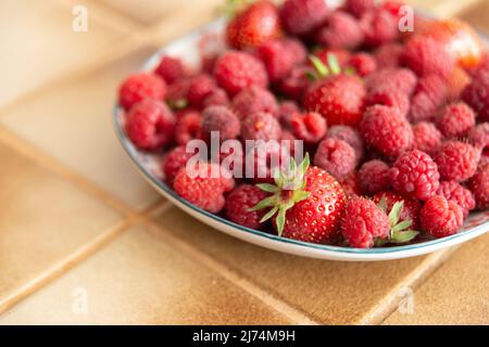 Teller mit frischen Erdbeeren und Himbeeren in einer Küche, in der rechten Ecke des Bildes Stockfoto