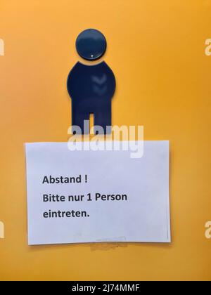 Hinweis mit der Aufschrift 'Abstand! Bitte geben Sie ein, dass nur 1 Personen an der Toilettentür des Herrenzimmer in Deutschland hängen Stockfoto