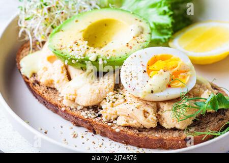 Ausgewogener Frühstückstoast mit Pastete, Avocado, Ei und Sprossen auf einem weißen Teller, Nahaufnahme. Stockfoto