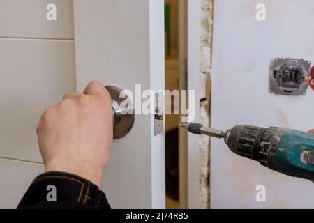 Der Schlosser hält den Schraubendreher bei der Installation des neuen Haustürschlosses Stockfoto