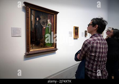 National Gallery London England April 2022 Besucher kehren nach London zurück, nachdem die Covid-Sperrbeschränkungen hier in der National Gallery am Trafalgar Square im Zentrum von London zwei Jahre lang gelten. Besucher bewundern das Arnolfini-Porträt (oder die Arnolfini-Hochzeit, die Arnolfini-Ehe, das Porträt von Giovanni Arnolfini und seiner Frau oder andere Titel), ein Ölgemälde des altniederländischen Malers Jan van Eyck aus dem Jahr 1434 auf Eichenholz. Es bildet ein vollständiges Doppelporträt, das vermutlich den italienischen Kaufmann Giovanni di Nicolao Arnolfini und seine Frau in ihrem Wohnsitz an der FLE darstellt Stockfoto