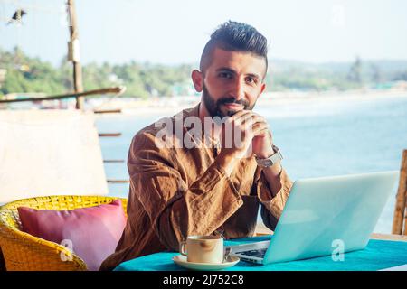 Attraktiver ägyptischer Arbeiter benutzt Computer in einer Cafeteria mit Meereshintergrund Stockfoto