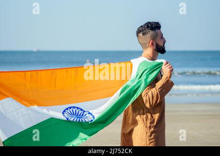 Indischer junger Mann mit indischer Tricolor-Flagge im Freien in der Nähe des Strandes, konzeptuelles Bild für den tag der republik oder zur Begrüßung am Tag der Unabhängigkeit Stockfoto