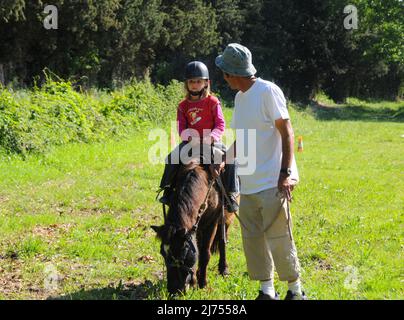 Junges Mädchen Reiten poney mit Vater hilft am sonnigen Tag Hobby oder Aktivität während der Ferien. Stockfoto