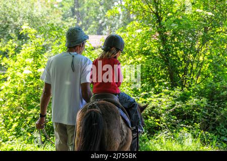 Junges Mädchen Reiten poney mit Vater hilft am sonnigen Tag Hobby oder Aktivität während der Ferien. Stockfoto