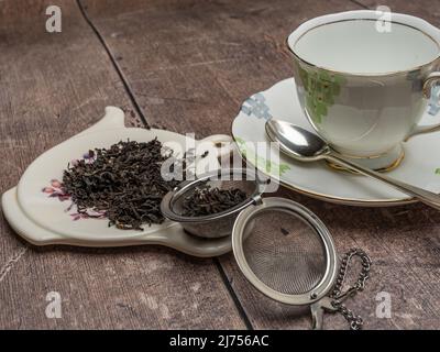 Englisches Frühstück schwarzer Tee in einem antiken Mesh-Sieb Porzellan Tasse und Untertasse und Silberlöffel serviert. Stockfoto