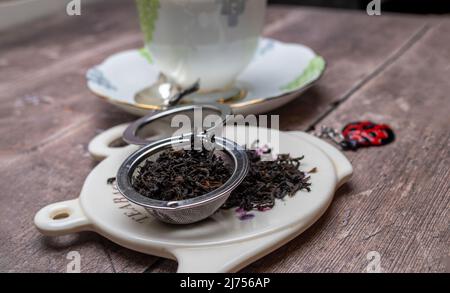 Ausgewählte Nahaufnahme auf Edelstahl-Mesh-Teesieb mit getrocknetem schwarzem Tee Stockfoto