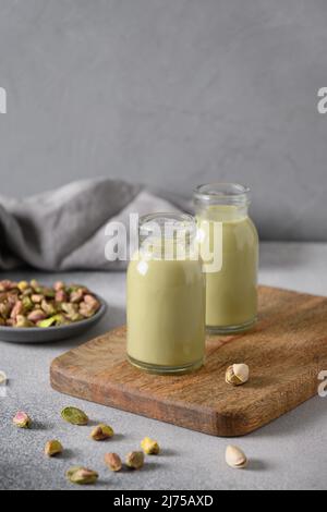 Pistazien-Milch in Flaschen auf grauem Hintergrund. Laktosefrei. Vegane nussige Milch auf pflanzlicher Basis. Vertikales Format. Stockfoto