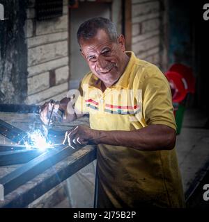 Alexandria, Ägypten - 21. Dezember 2021: Ein Mann arbeitet mit einem Schweißer in einer kleinen Straßenwerkstatt ohne Maske, lächelnd Stockfoto