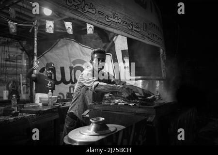 Alexandria, Ägypten - 21. Dezember 2021: Ein Mann frittiert nachts Fisch im Straßenrestaurant, Schwarzweißfoto Stockfoto