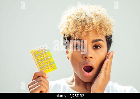 Schöne Überraschung afroamerikanische Frau hält Geburtenkontrolle Tablette und offenen Mund becouse sie vergessen, die Pillen rechtzeitig zu nehmen. Zahnschmerzen Konzept Stockfoto