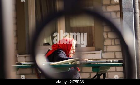 Defokussieren sie die ältere ukrainische Frau in einem roten Schal mit Krücken, die draußen sitzen. Frau 85 Jahre alt. Einzelperson. Nahaufnahme. Verschwommen. Traurige Menschen. Demen Stockfoto