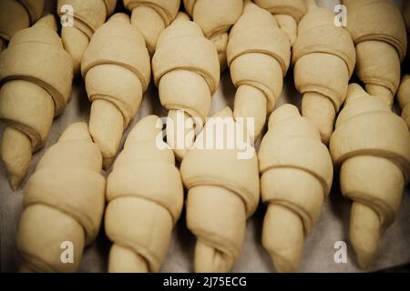 Croissants, die auf einer Pfanne sitzen und darauf warten, in einer Bäckerei in den Ofen gestellt zu werden Stockfoto