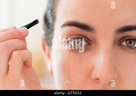 Nahaufnahme Makroportrait mit gelben Augen Frau weint vor Schmerzen mit einem Tränenabfall von ihrem Gesicht, nachdem sie ihre Augenbrauen ausgerupft hat Stockfoto