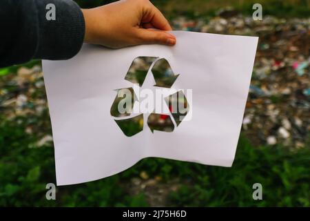 Defokussieren Hand halten Papier mit dem Logo des Recyclings auf Müllabfuhr Hintergrund. Recyclingkonzept. Verschmutzung des Planeten. Nicht fokussiert Stockfoto