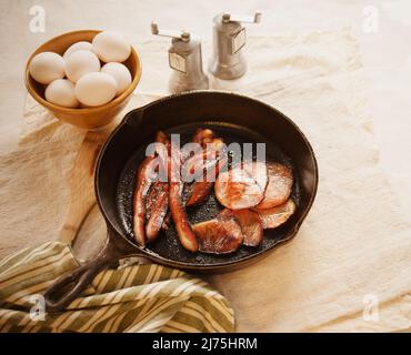 Gusseiserne Pfanne mit Speck und Schinken und einer Schüssel Eier Stockfoto