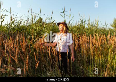 Unschärfe-Außenportrait einer schönen blonden Frau mittleren Alters in der Nähe von Schilf- und Pampagras. Jugend, Liebe, Mode, Romantik und Lifestyle-Konzept. 40s Stockfoto